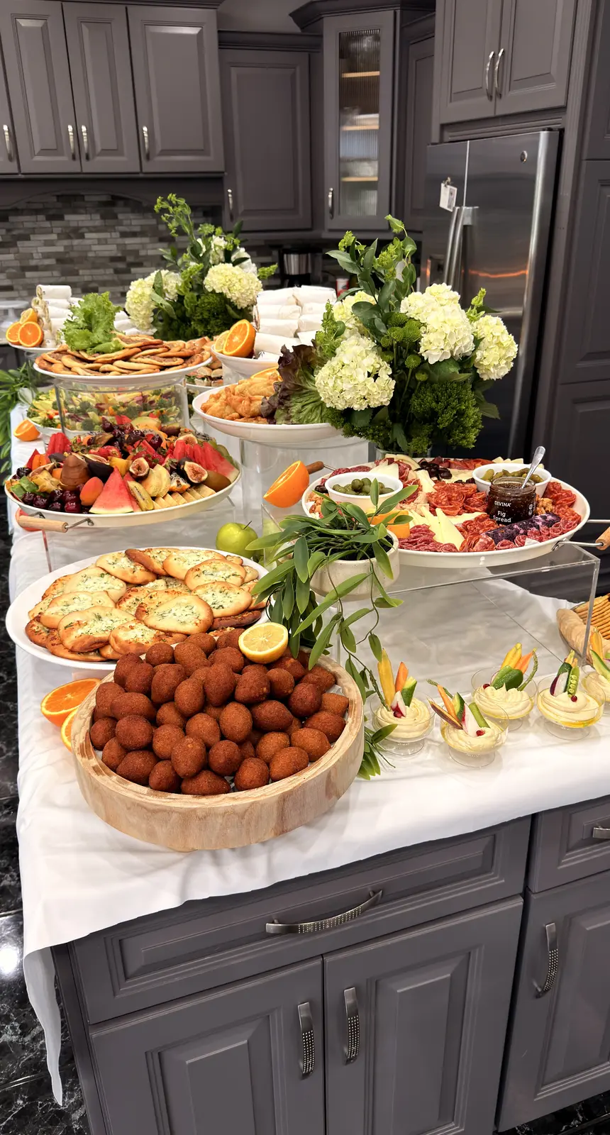 Noosh Catering outdoor grazing table with falafel, crackers, fresh fruit and white hydrangeas.