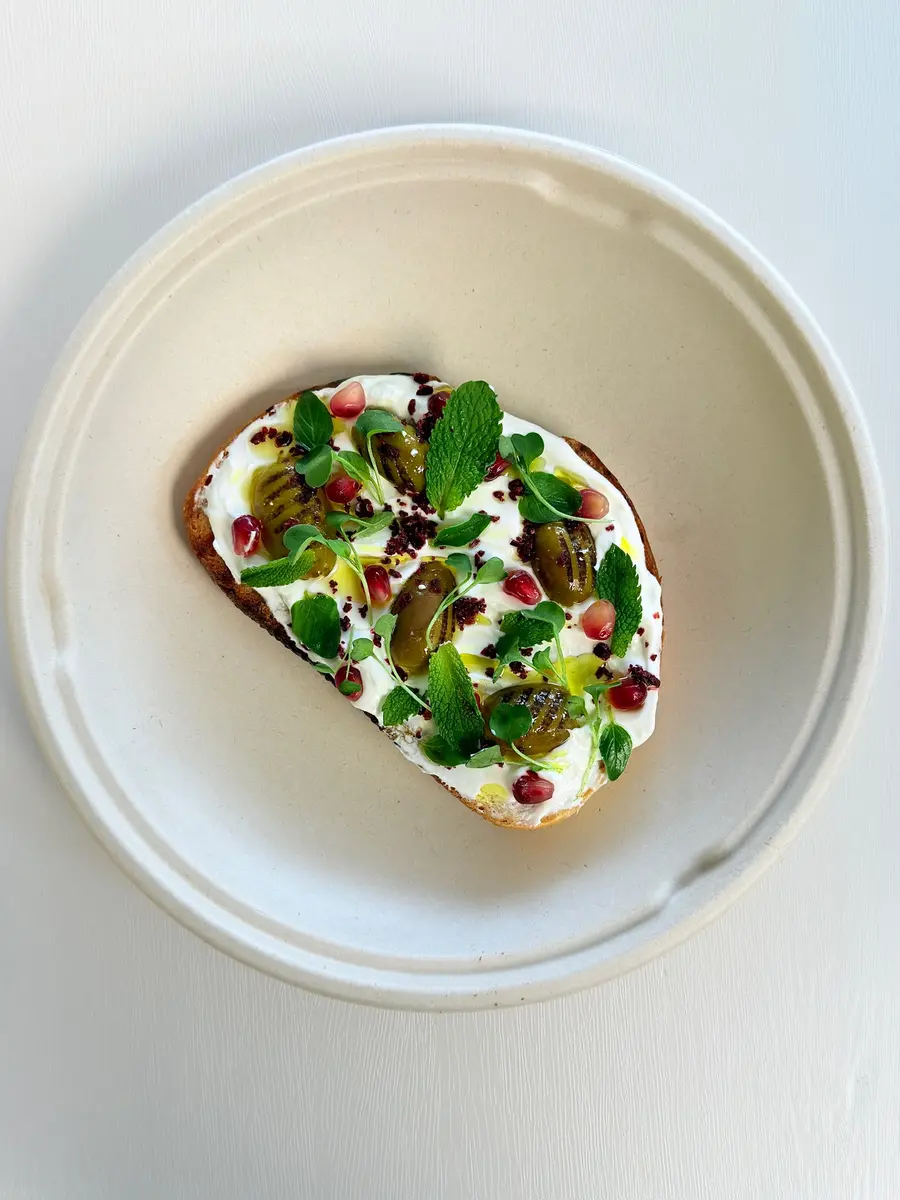 Labneh toast with fresh herbs and green olives on sourdough at Fil Fil Mediterranean in Homer Glen, IL.